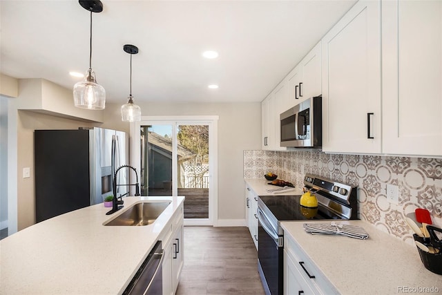 kitchen with appliances with stainless steel finishes, a sink, wood finished floors, baseboards, and backsplash