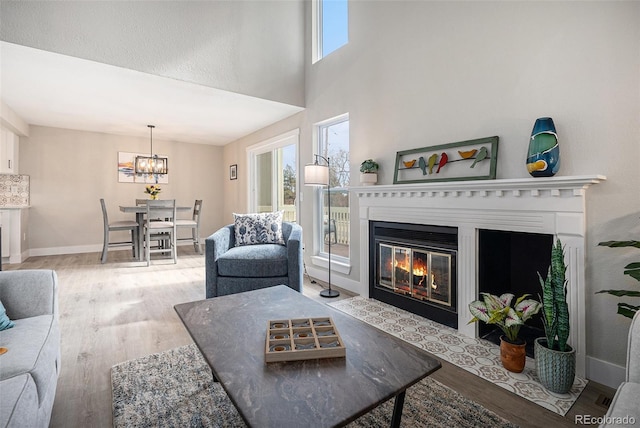 living area featuring wood finished floors, a fireplace with flush hearth, a chandelier, baseboards, and a high ceiling