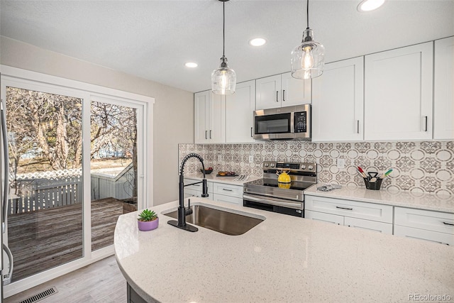kitchen featuring stainless steel appliances, a sink, recessed lighting, light stone countertops, and pendant lighting