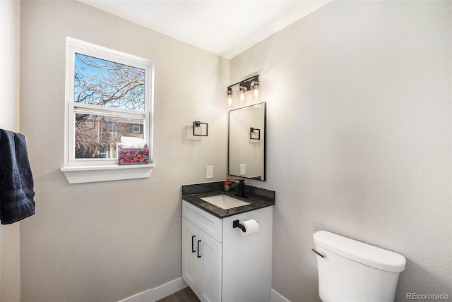 half bathroom with vanity, toilet, and baseboards