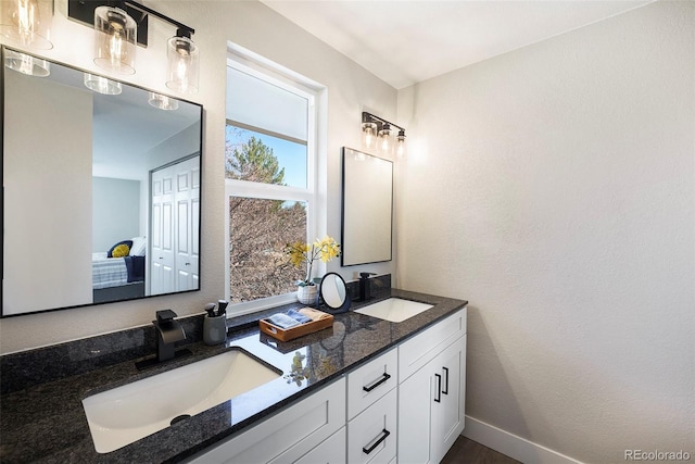 bathroom with double vanity, a textured wall, and baseboards