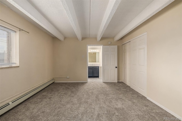 unfurnished bedroom with baseboard heating, beam ceiling, connected bathroom, a textured ceiling, and light carpet