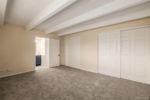 unfurnished bedroom featuring beamed ceiling, carpet floors, two closets, and a textured ceiling