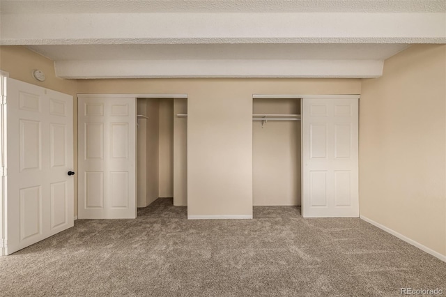 unfurnished bedroom with two closets, beamed ceiling, and carpet