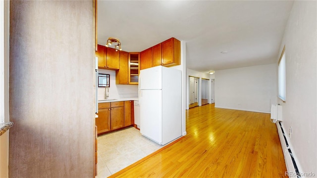 kitchen with a baseboard radiator, sink, white appliances, and light hardwood / wood-style floors