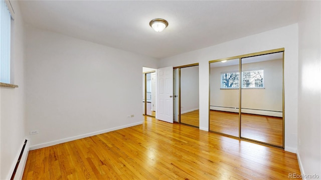 unfurnished bedroom featuring a baseboard heating unit, hardwood / wood-style floors, and multiple closets