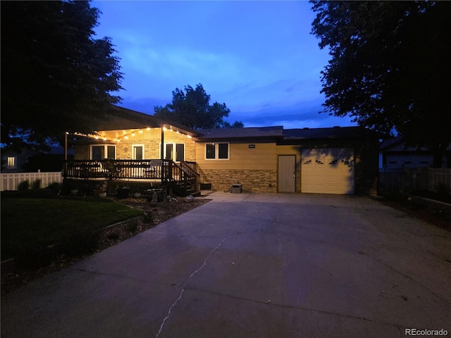 720 W 4th St, Julesburg, CO 80737 - back of house at dusk featuring stone siding, concrete driveway, a garage, and a deck