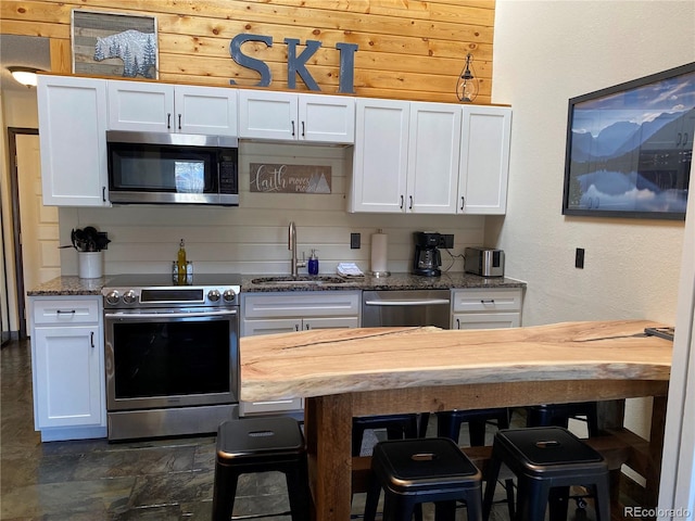 kitchen with stainless steel appliances, butcher block counters, white cabinetry, a sink, and a kitchen breakfast bar