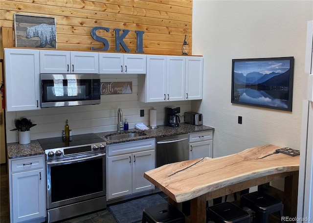 kitchen featuring appliances with stainless steel finishes, dark stone countertops, a sink, and white cabinetry