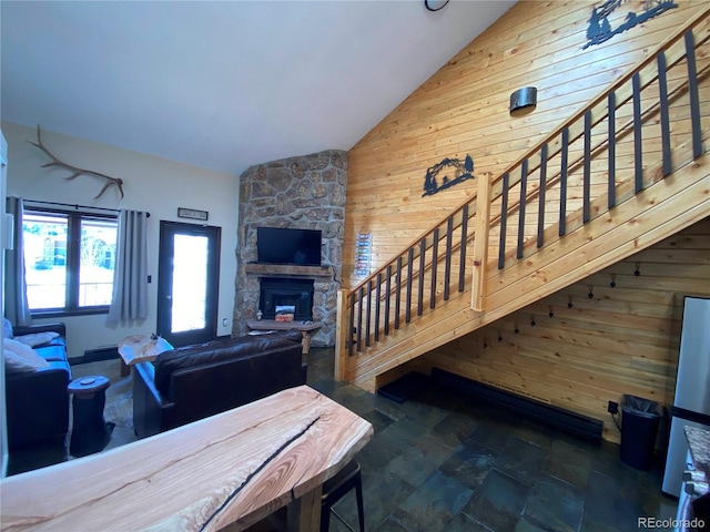 living room with vaulted ceiling, a stone fireplace, stairway, and wood walls