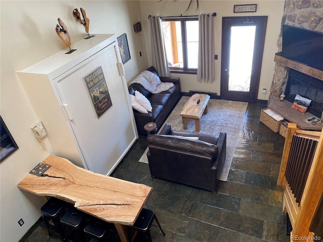 living area featuring stone finish floor, a fireplace, and baseboards