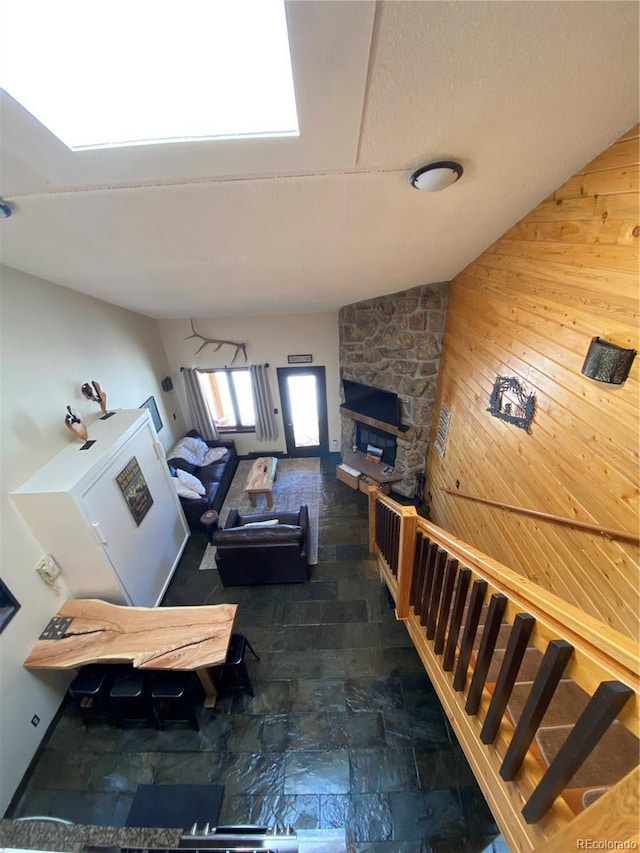 living room with a fireplace, stairway, stone finish flooring, wood walls, and vaulted ceiling