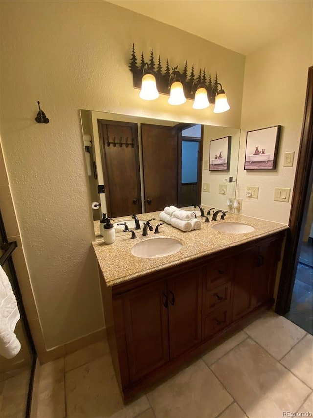 bathroom featuring a textured wall, double vanity, tile patterned flooring, and a sink