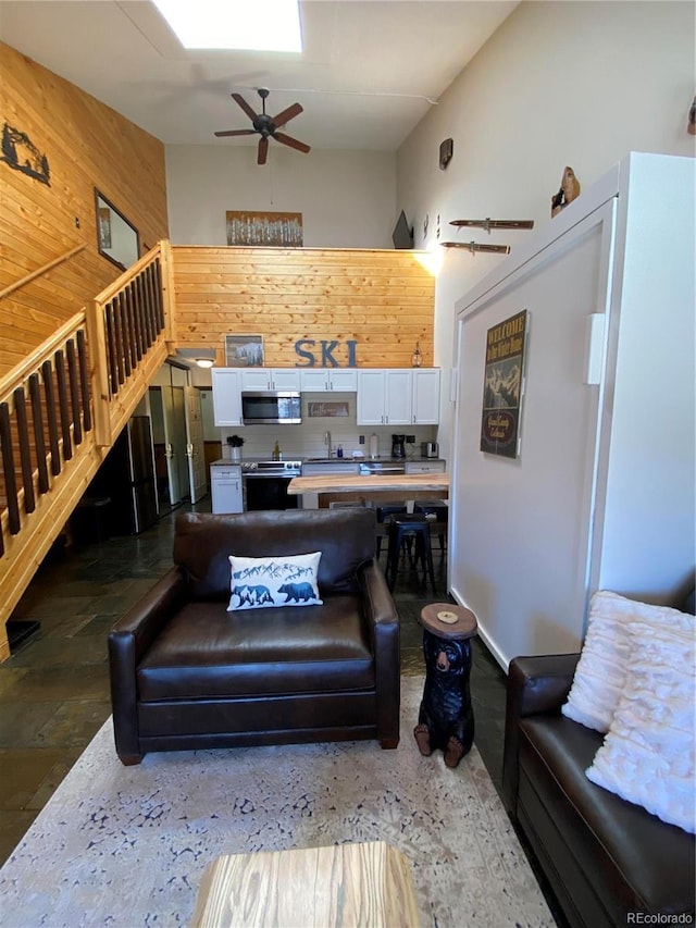 living area with wood walls, ceiling fan, a high ceiling, and stairway