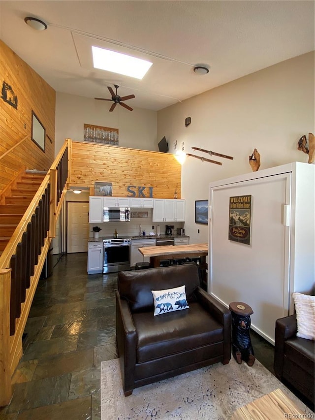 living area featuring stone finish flooring, ceiling fan, wooden walls, and a towering ceiling