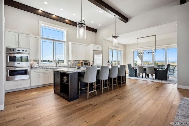 kitchen with light hardwood / wood-style floors, a center island, white cabinetry, stainless steel appliances, and decorative light fixtures