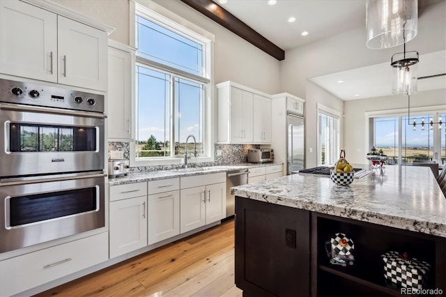 kitchen with beamed ceiling, stainless steel appliances, light wood-type flooring, and white cabinetry