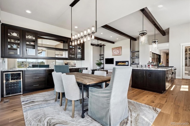 dining area featuring bar, light hardwood / wood-style floors, beamed ceiling, and wine cooler