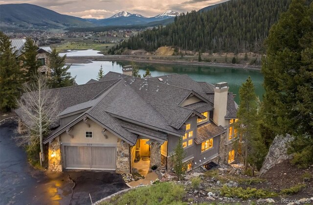 309 Eastridge Dr, Dillon, CO 80435 - view of front of house with a chimney, stone siding, a shingled roof, and a water and mountain view