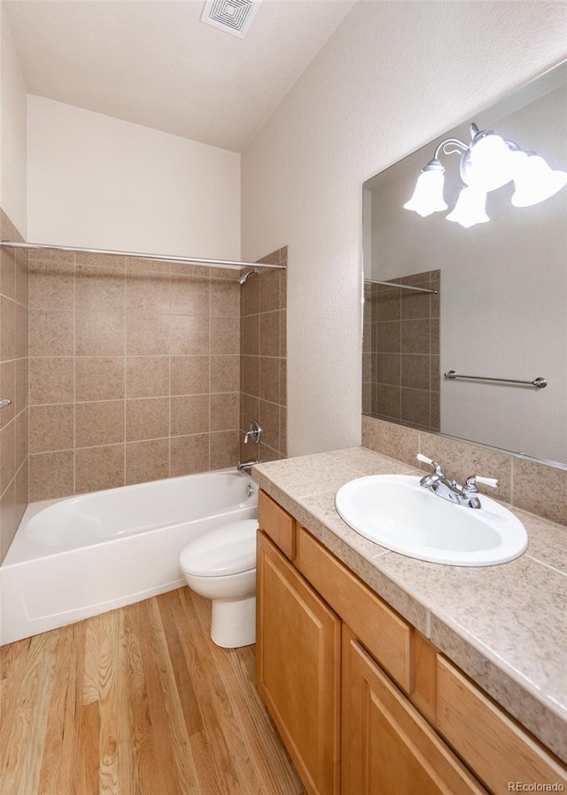 full bathroom featuring hardwood / wood-style floors, tiled shower / bath, vanity, and toilet