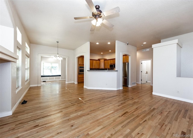 unfurnished living room featuring ceiling fan with notable chandelier and light wood-type flooring