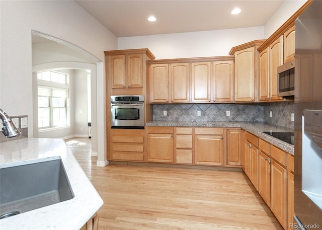 kitchen featuring appliances with stainless steel finishes, sink, light hardwood / wood-style flooring, and tasteful backsplash