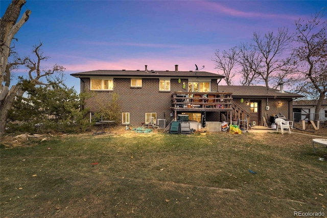 back house at dusk featuring a wooden deck and a yard