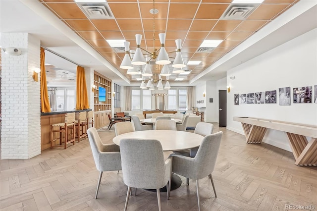 dining space featuring light parquet flooring, a tray ceiling, plenty of natural light, and brick wall