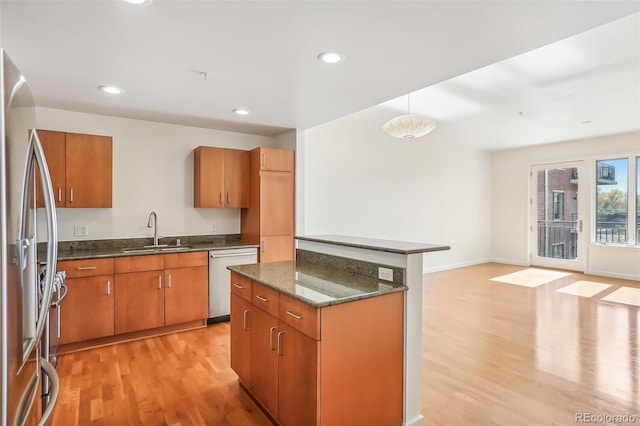 kitchen with sink, appliances with stainless steel finishes, light wood-type flooring, and dark stone countertops