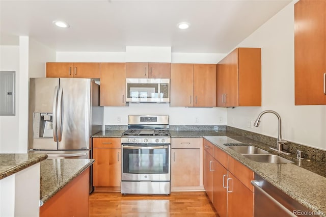 kitchen with dark stone countertops, stainless steel appliances, sink, and light wood-type flooring