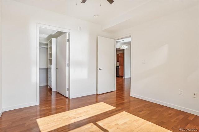 unfurnished bedroom featuring hardwood / wood-style floors, a walk in closet, a closet, and ceiling fan