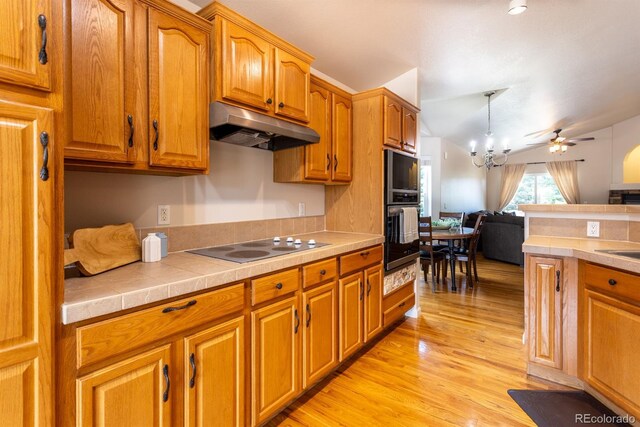 kitchen with black electric cooktop, light hardwood / wood-style flooring, ceiling fan with notable chandelier, decorative light fixtures, and tile countertops