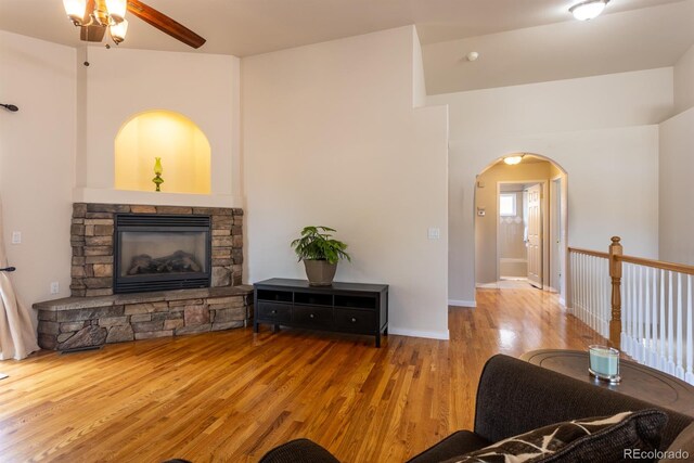 living room with a stone fireplace, wood-type flooring, and ceiling fan