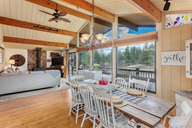 dining room with a wood stove, vaulted ceiling with beams, plenty of natural light, and light wood-style floors