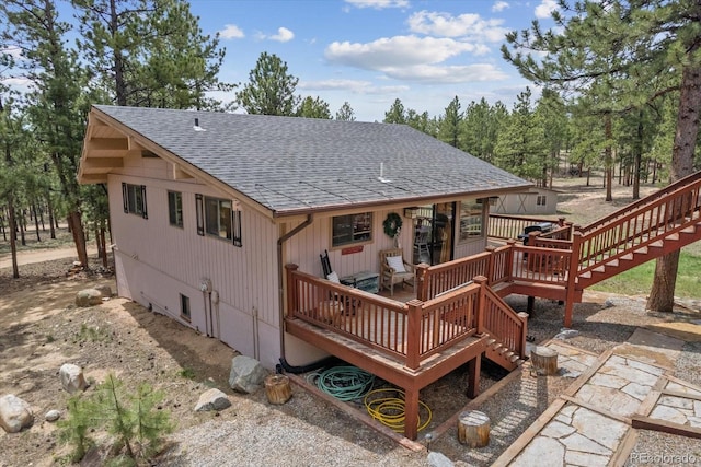 rear view of property featuring a shingled roof, stairway, and a deck