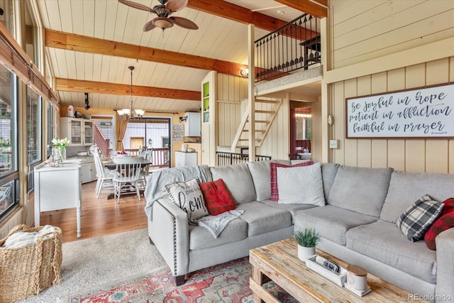 living area featuring ceiling fan with notable chandelier, lofted ceiling with beams, wood finished floors, stairway, and wooden walls
