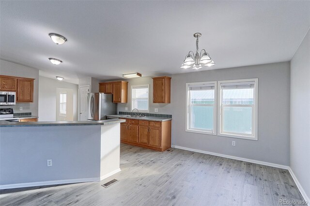 kitchen with stainless steel appliances, sink, decorative light fixtures, light hardwood / wood-style flooring, and a chandelier