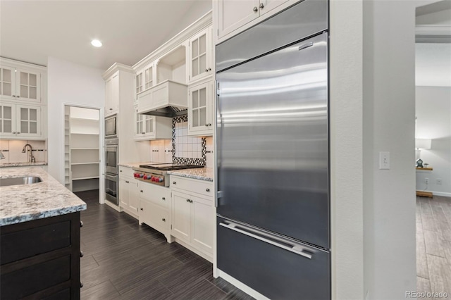 5980 Dunraven Ct, Golden, CO 80403 - kitchen featuring built in appliances, backsplash, light stone countertops, white cabinets, and dark wood-style flooring