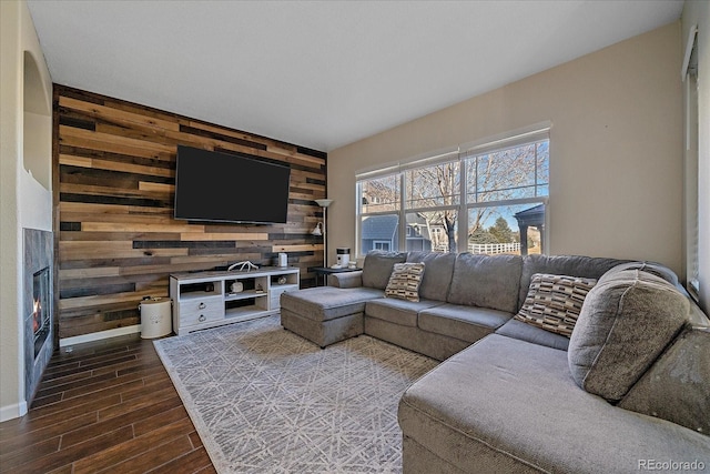 living room featuring wood walls, wood tiled floor, an accent wall, and a lit fireplace