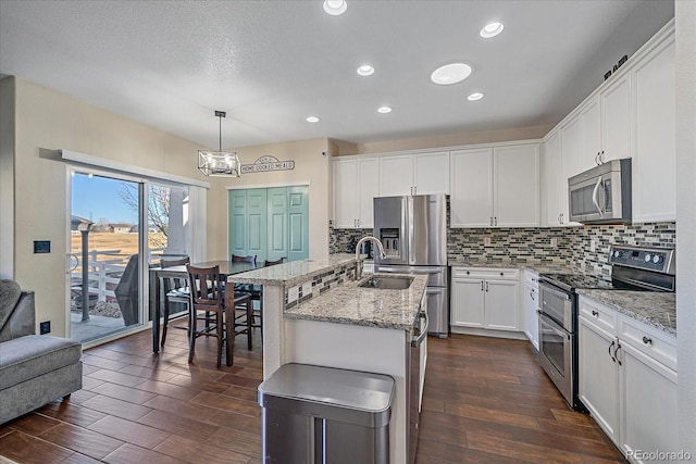 kitchen featuring dark wood-style floors, stainless steel appliances, tasteful backsplash, a kitchen island with sink, and white cabinetry