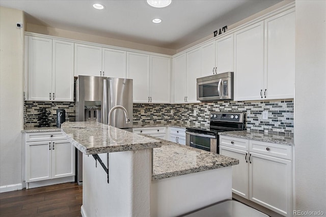 kitchen with stainless steel appliances, dark wood-type flooring, a center island with sink, and white cabinetry