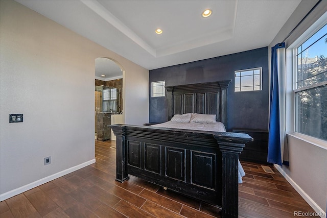 bedroom with wood tiled floor, arched walkways, a raised ceiling, and baseboards