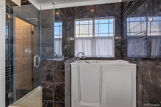 bathroom featuring a garden tub, a shower stall, washer / clothes dryer, and tile walls