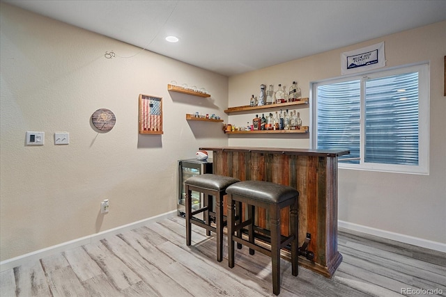 bar featuring a dry bar, light wood-style flooring, baseboards, and beverage cooler