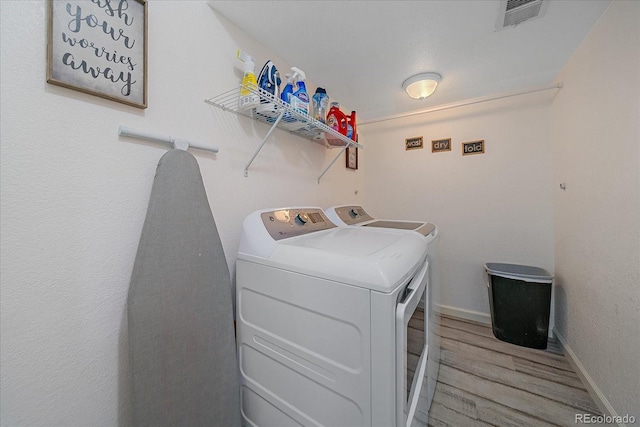 laundry area with washer and clothes dryer, visible vents, light wood-type flooring, laundry area, and baseboards