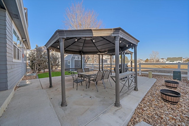 view of patio / terrace with an outbuilding, fence, outdoor dining area, a gazebo, and a shed