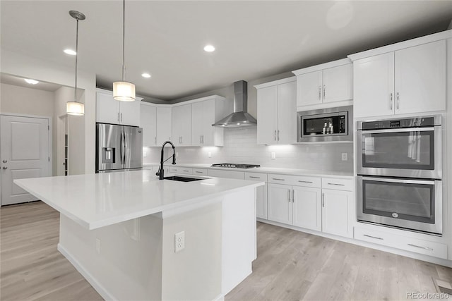 23895 E Rocky Top Pl, Aurora, CO 80016 - kitchen with wall chimney range hood, stainless steel appliances, a sink, a kitchen island with sink, and light wood finished floors