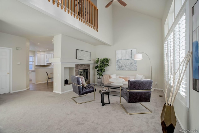 carpeted living room featuring a tiled fireplace, ceiling fan, and a high ceiling