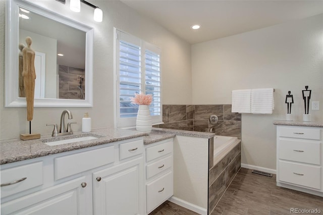 bathroom featuring a relaxing tiled tub, vanity, and hardwood / wood-style flooring