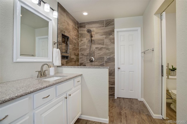 bathroom featuring wood-type flooring, tiled shower, vanity, and toilet